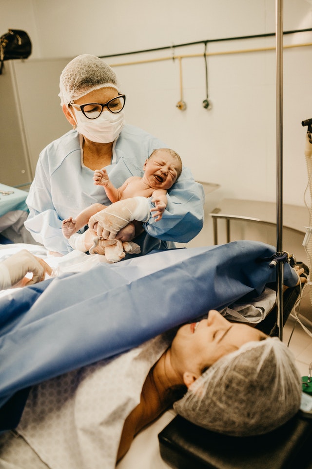 Uma médica segurando um Bebê recém nascido, mostrando para a mãe.